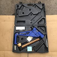 Open carrying case showing blue Campbell Hausfeld pneumatic flooring nailer, wooden mallet, box of nails and hex keys.