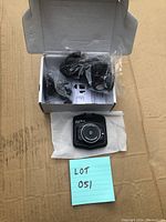 Photo of the dash cam placed on white tissue next to an open box containing cables and mounting clip.