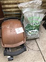 Closed Weber BBQ grill with two bags of decorative gravel behind it, showing brand label and lot tag.