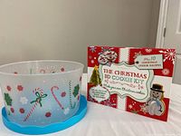 Photo of holiday-themed plastic container with blue lid and Christmas motifs, alongside the Christmas 3D cookie kit box showing festive graphics and text.