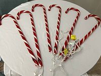 Six red and white striped candy cane lights with white wiring laid out on a white table.