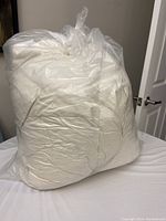 White feather bed mattress topper rolled and vacuum-sealed inside a clear plastic bag, displayed on a bed.