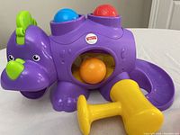 Purple Fisher-Price dinosaur toy with yellow hammer on a white surface.