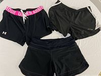Three pairs of black workout shorts laid on white background: Under Armour with pink waistband, Sweaty Betty black/grey shorts, and Lululemon shorts in front