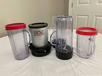 Magic Bullet blender base with 4 plastic cups and 2 blade attachments displayed on a flat surface in front of a door.