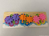 Photo showing the wooden toddler toy featuring six colorful butterfly-shaped gears mounted on a wooden base with painted decorative elements.