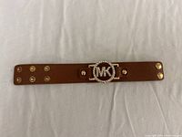 Photo of adjustable Michael Kors bracelet with brown leather strap and crystal-encrusted MK logo centerpiece.