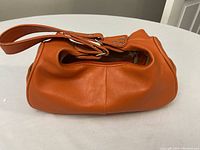 Side view of soft orange leather purse with single wide strap.