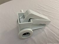 White plastic handheld Parmesan cheese grater with crank and drum mechanism on beige fabric surface.