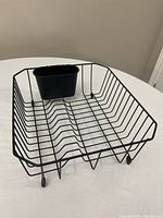 Small black wire dish drying rack on white table with a small black plastic utensil holder attached inside.