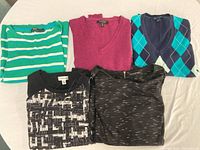 Set of five sweaters arranged flat on table, showing variety of colors and styles.