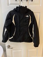 Front view of The North Face winter jacket in black with white accents, hung on a door.