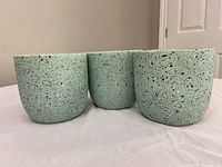 Three turquoise round flower pots with black speckled pattern on a white surface near a door.