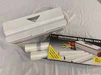 White electric vacuum sealer placed next to partial polyethylene rolls and original Salton refill pack box.