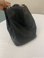 Side view of the smooth black leather-like backpack showing its shape and structure.