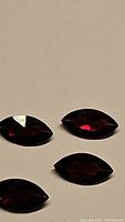 Close-up photo of four fancy-cut marquise-shaped almandine garnets with deep red color and glossy facets.