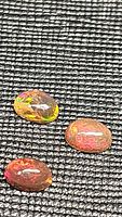 Three oval cabochon chocolate opals displayed on black textured background showing colorful internal flashes