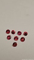 Photo of eight round cut maple fire red sapphires arranged on a flat surface, showing color and size consistency.