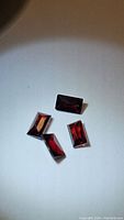 Four fancy baguette cut almandine garnet gemstones arranged on a white surface showing deep reddish-brown color and faceting detail.