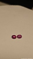 Two natural oval cabochon pink sapphires displayed on a neutral surface.