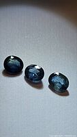 Three oval cut natural blue sapphires with teal green tones shown on a light background, highlighting their size and color.