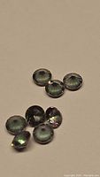 Top view photo showing seven round Mystic Topaz gemstones with visible rainbow coloration effects under light.