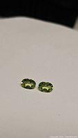 Two apple green oval Peridot gemstones placed side by side on a neutral background, showing front view.