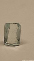 Close-up photo of the rectangular sky blue aquamarine gemstone standing on edge against a plain background showing clarity and cut.
