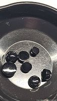 Six polished natural black onyx round cabochon gemstones in black tray, showing smooth glossy surfaces and opaque black color.