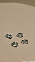 Four pear shaped sky blue topaz gemstones on flat neutral background showing cut and color.