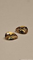 Pair of pear cut natural citrine gemstones placed on a beige background showing facets and color.
