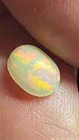 Close-up photo of an oval cabochon Ethiopian opal gemstone displaying a play of rainbow colors on a person's finger.