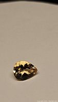 Close-up photo of a pear-shaped natural golden citrine gemstone lying on a neutral background, showing facets and clarity.