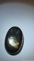 Front view of the oval cabochon golden pyrite gemstone showing metallic gold luster and polished surface.