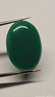 Close-up photo of the smooth oval green onyx cabochon held with tweezers, showing polished surface and color.