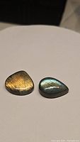Two pear-shaped natural labradorite cabochons showing golden and blue flashes, placed side by side on a white surface.