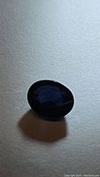 Natural oval cut deep midnight blue sapphire gemstone photographed on a white background showing color and faceting.