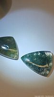 Two moss agate cabochons displayed on a white background, showing clear moss-like inclusions and polished surfaces.