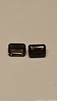 Pair of natural emerald cut smokey quartz gemstones placed on a neutral background showing color and cut detail.