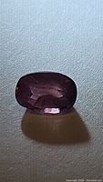 Oval cut natural pink purple sapphire gemstone, approx 0.75 carats, shown on white textured background to display color and facets.