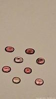Eight pink tourmaline gemstones of various pink shades displayed scattered on a plain background showing cut, clarity and colors.