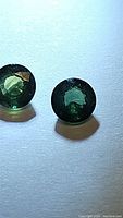 Two round-cut natural green sapphires with deep green color and clarity shown on white background.