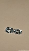 Pair of oval cut natural sky blue topaz gemstones on a neutral background, showing clarity and faceted cuts.