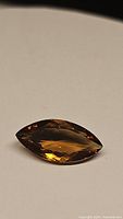 Photo shows a marquis cut Madeira citrine gemstone with a deep cognac color. The gem displays faceting and excellent luster on a white background.