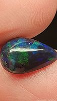 Close-up photo of untreated black Ethiopian opal with pear shape, showing vibrant blue and green flashes.