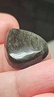 Close-up image showing the smooth, polished pear-shaped black obsidian cabochon with visible silver sheen reflecting light.