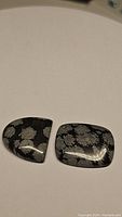 Top view of two cabochon-shaped natural snowflake obsidian stones showing characteristic crystal inclusions in black volcanic glass.