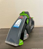 Close-up of the front of the handheld BISSELL Pet Stain Eraser showing the clear nozzle and pull tab.