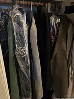 Clothes hanging on a closet rod including coats and jackets, some covered in clear plastic.