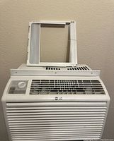 Front view of LG window air conditioner with control dial and window mounting frame on top.